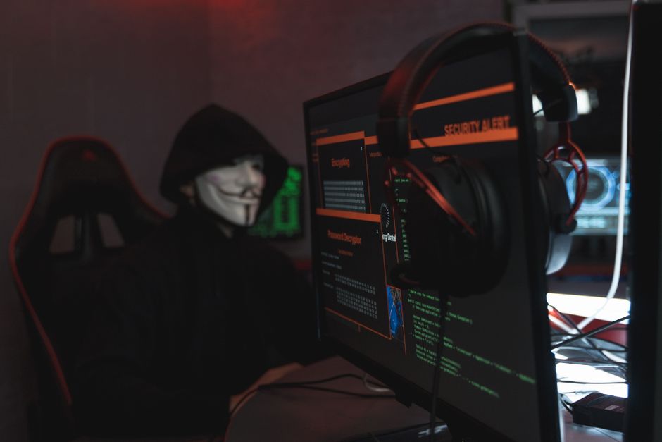 A staged cybersecurity scene with a masked person beside computer screens